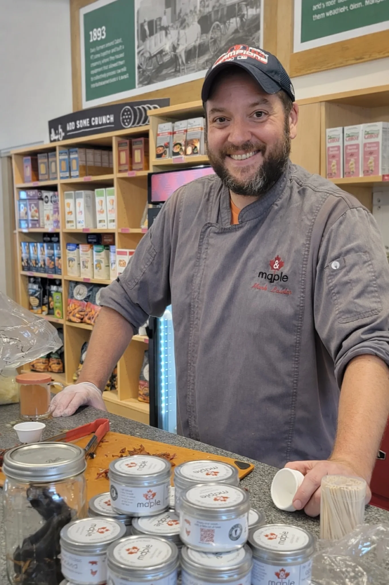 Mark Lawler presenting tins of & Maple seasoning at a retail counter.
