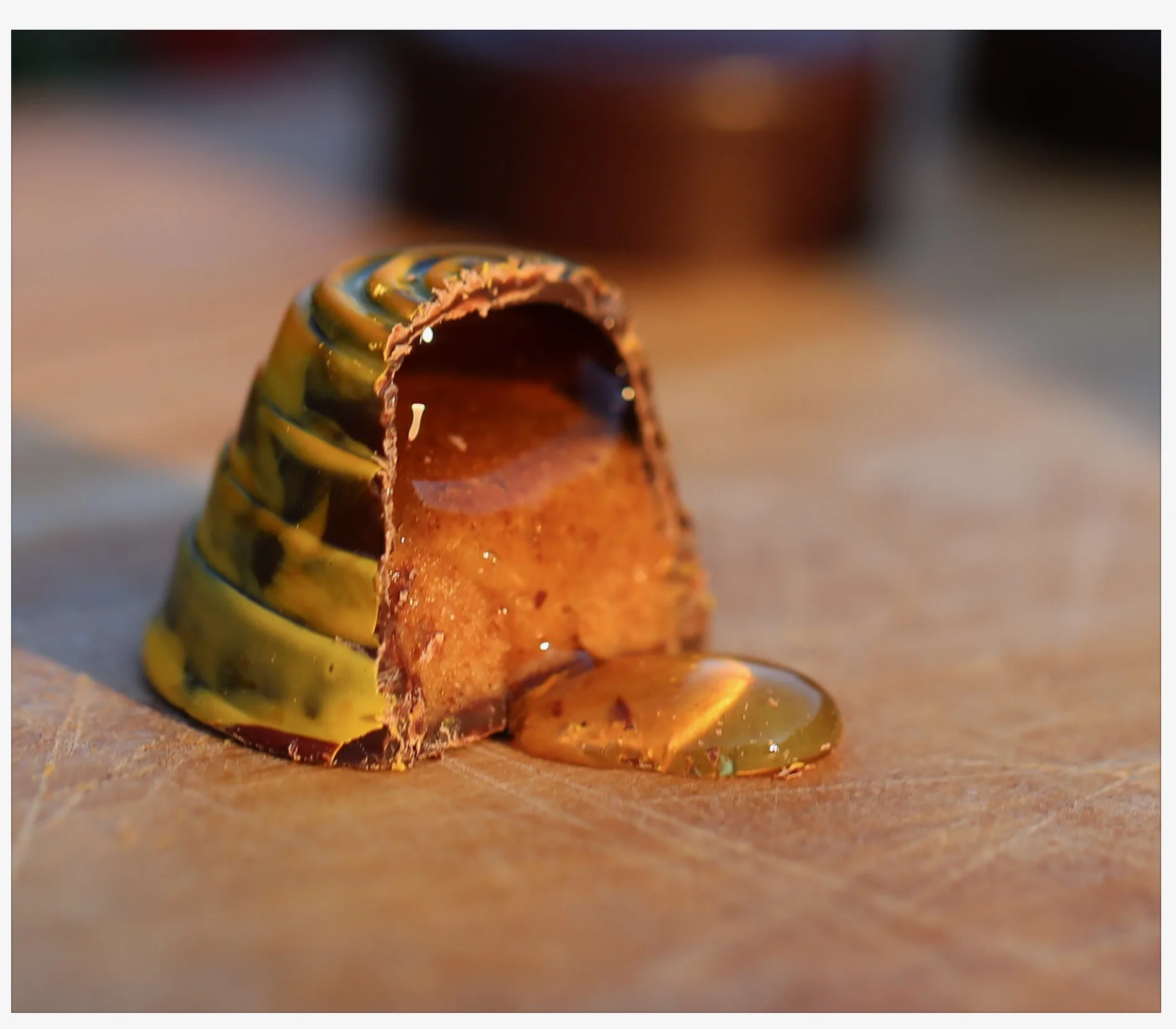 A small gold-and-green striped bonbon cut open, with honey flowing from its center.